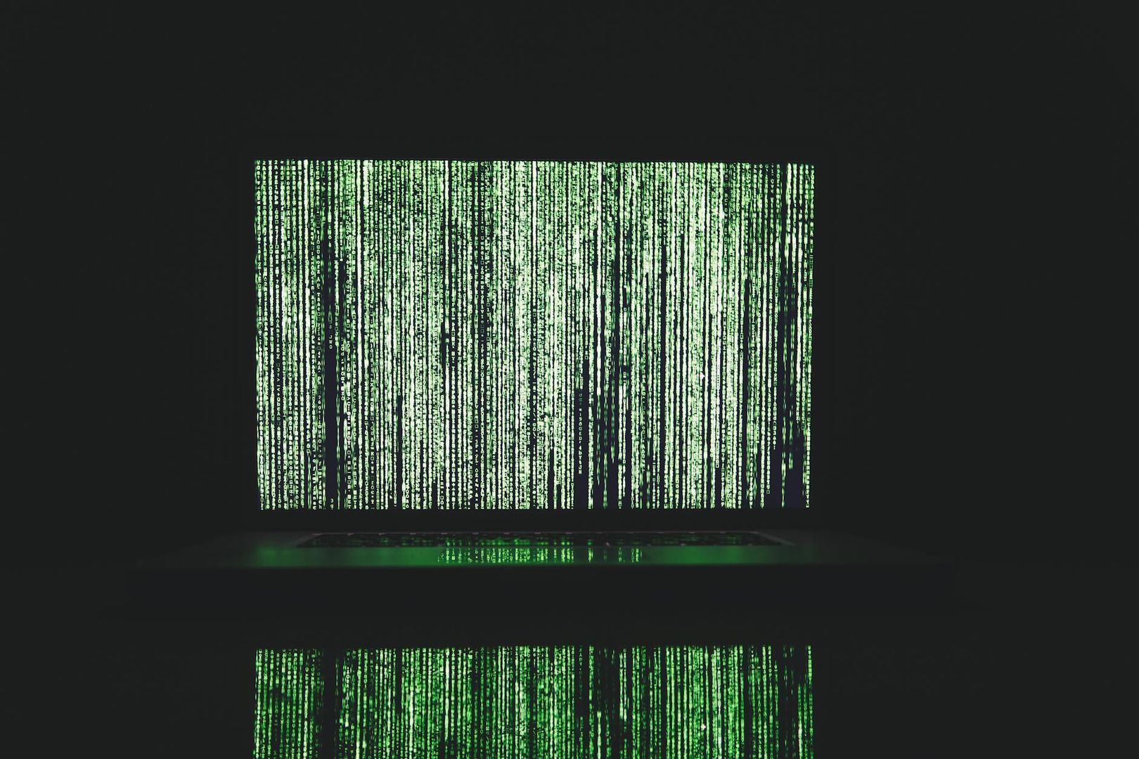 Öppen bärbar dator med grön fallande Matrix-kod som speglas på ytan framför.